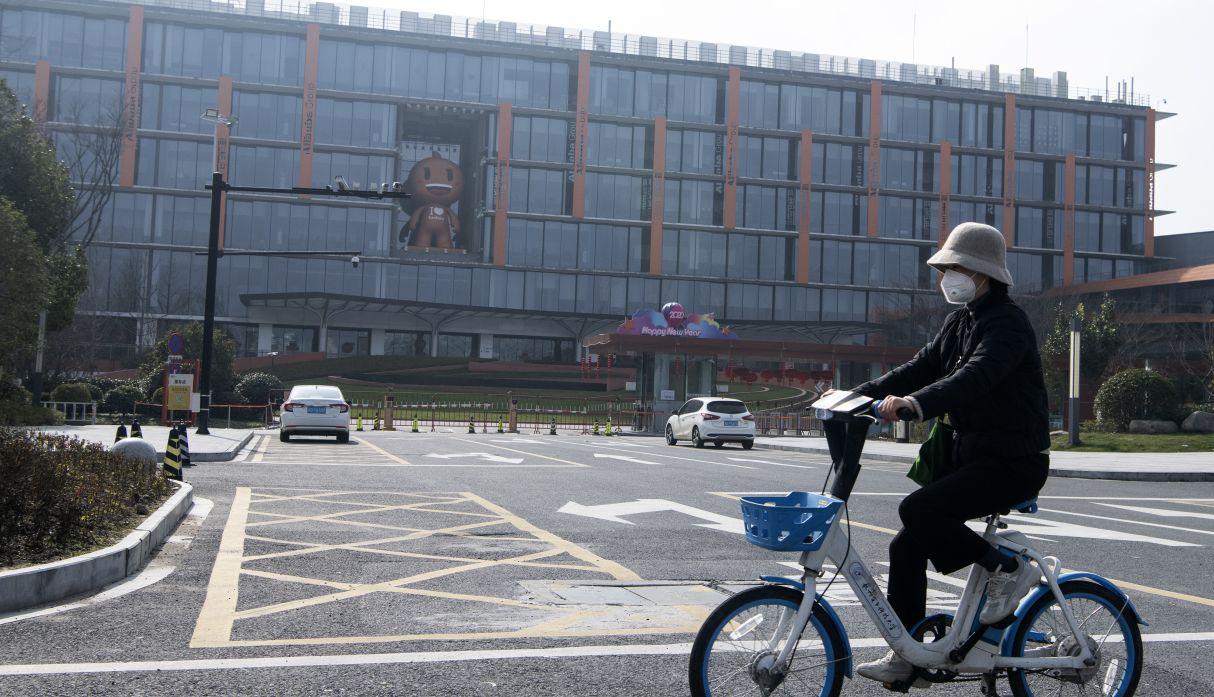 Una mujer con su mascarilla pasa en bicicleta por la sede de Alibaba en Hangzhou. (AFP).
