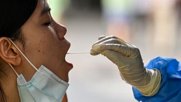 Un trabajador de la salud toma una muestra de hisopo de una mujer para la prueba del coronavirus Covid-19 en el distrito de Huangpu, China, el 17 de agosto de 2022. (Héctor RETAMAL / AFP).
