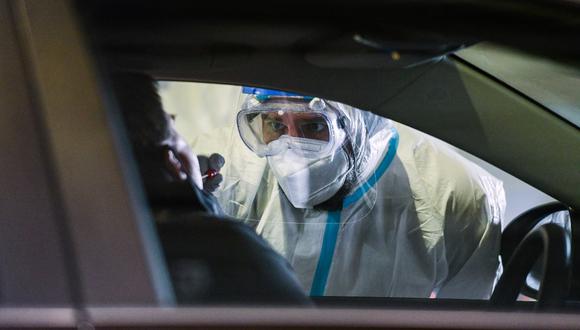 A helper in a protective suit takes a sample from the mouth of the driver of a vehicle at a coronavirus testing station set up at the former Guetersloh military airport on June 30, 2020. - German Armed Forces and aid organizations have set up a smear station, where people can be tested for Covid-19 after the coronary outbreak at the Toennies meat plant. (Photo by Ina FASSBENDER / AFP)