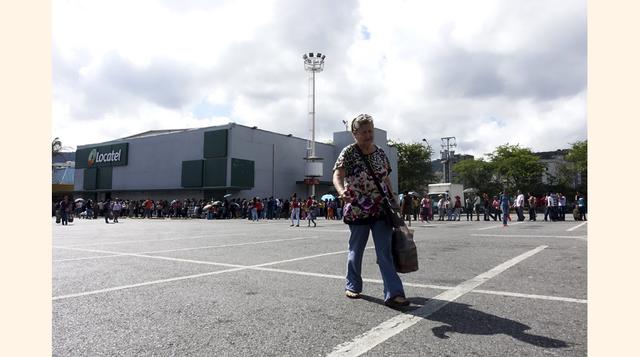 Una mujer lleva una bolsa de plástico mientras otras personas hacen cola para comprar artículos de primera necesidad en un supermercado Makro en Caracas. Los venezolanos pasan horas haciendo colas para comprar productos que van desde la harina de maíz has