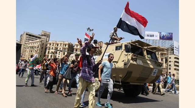 Ciudadanos egipcios ondean su bandera nacional y caminan junto a un vehículo militar durante la celebración de inauguración del Canal de Suez en la ciudad de El Cairo. La espectacular inauguración buscó fortalecer la posición internacional de Egipto, con 