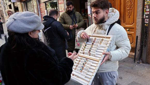 Una persona compra billetes de lotería de Navidad a un vendedor ambulante frente al popular establecimiento de lotería 'Dona Manolita' el 18 de diciembre de 2023 en el centro de Madrid (Foto: Thomas Coex / AFP)