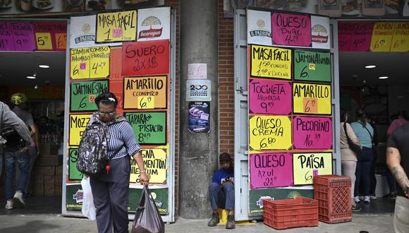 Una mujer sostiene una bolsa de supermercado frente a una tienda que muestra carteles con precios en dólares en el mercado municipal de Quinta Crespo en Caracas el 15 de diciembre de 2022. (Foto de Federico PARRA / AFP)