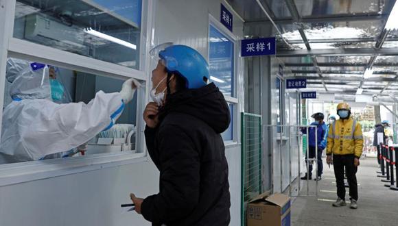 Un trabajador médico con traje protector recoge un hisopo de un repartidor para realizar pruebas de ácido nucleico en un hospital en medio del brote de la enfermedad por coronavirus (COVID-19), en el distrito de Changning de Shanghái, China.