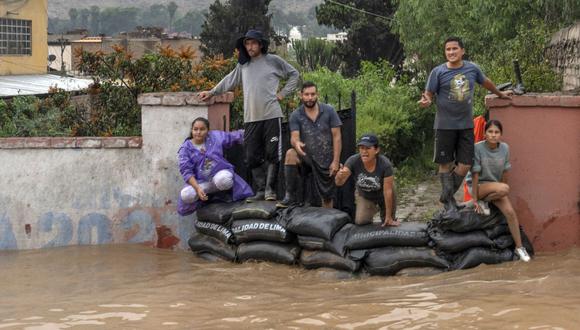 La gente mira detrás de sacos de arena mientras el agua inunda la principal vía de acceso de Lima al interior del país en los Andes tras las fuertes lluvias en Chaclacayo, al este de Lima, Perú, el 15 de marzo de 2023. (Foto: AFP)