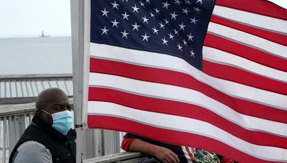 Un hombre con una máscara facial se sienta cerca de una bandera estadounidense en un muelle en Coney Island en medio de la pandemia de coronavirus, en Nueva York. (Foto: AFP/Bryan R. Smith)