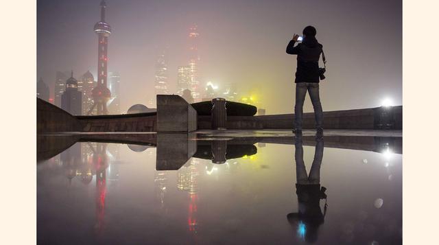 Un hombre usa su teléfono móvil para tomar fotografías de la zona financiera del nuevo distrito de Pudong en un día con mucho smog en Shanghai. Una niebla pesada y espesa envolvió a muchos lugares del norte y el este de China. (Foto: REUTERS)