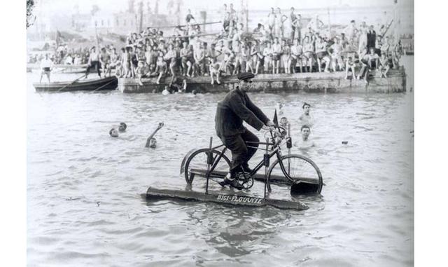 Manuel Pérez, inventor de la bici flotante, pasea por el río mientras se celebra la cucaña en sevilla en 1927