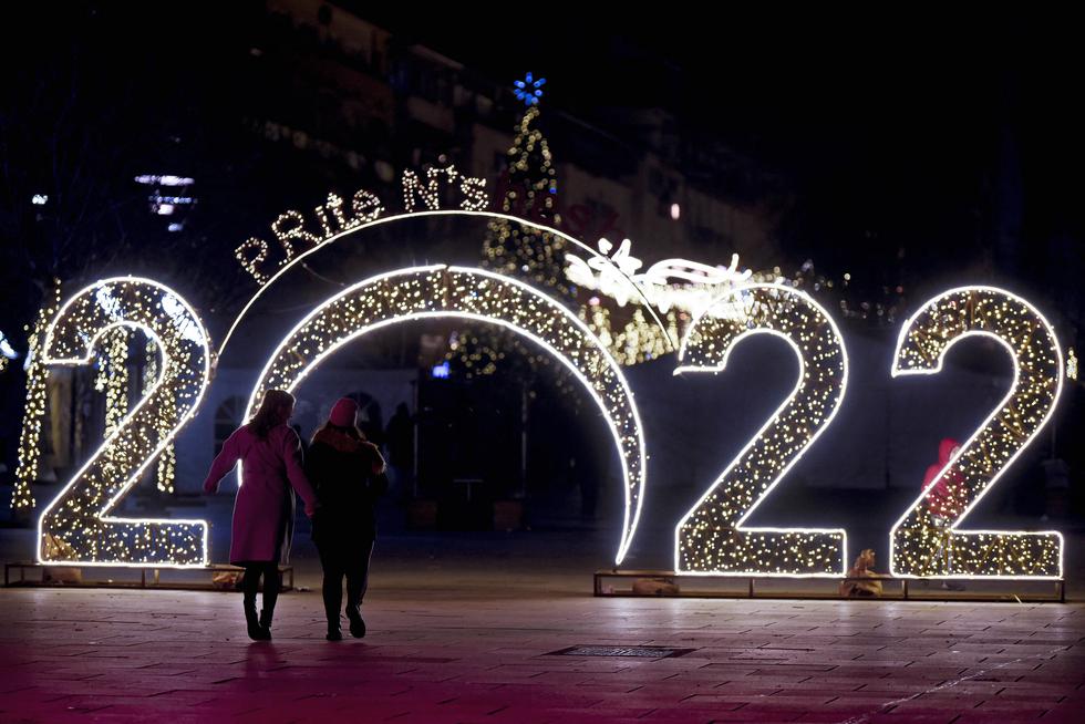 Las mujeres caminan frente a un letrero de 2022 exhibido en el centro de Pristina el 30 de diciembre de 2021, antes de las celebraciones del Año Nuevo en Kosovo. (Foto de Armend NIMANI / AFP)