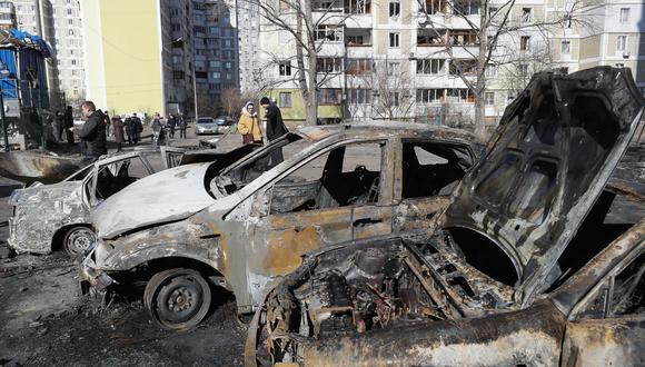 La gente pasa junto a carros quemados un día después de un bombardeo en una zona residencial de Kiev. (EFE/EPA/SERGEY DOLZHENKO)