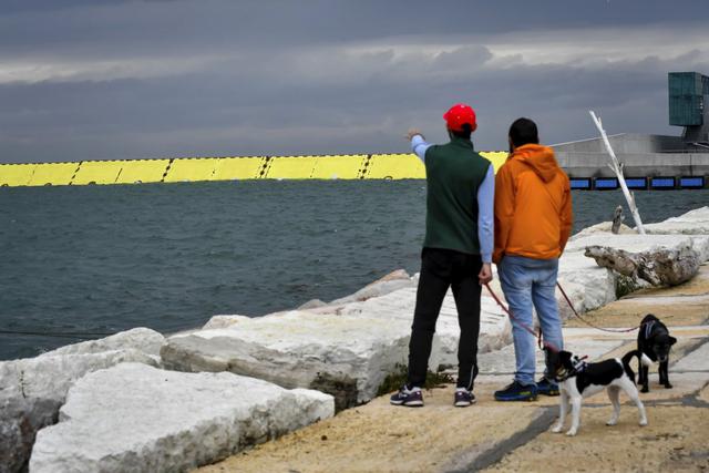 Las personas observan las barreras amarillas que se levantan durante la marea alta en Venecia, en el norte de Italia. (Claudio Furlan/LaPresse/AP).