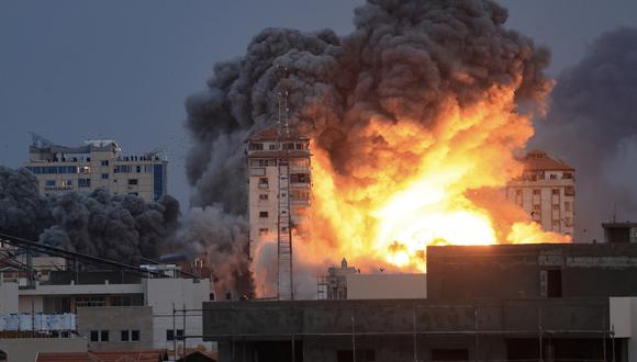 Personas paradas en una azotea observan cómo una bola de fuego y humo se eleva sobre un edificio en la ciudad de Gaza el 7 de octubre de 2023 durante un ataque aéreo israelí. (Foto de MAHMUD HAMS / AFP)