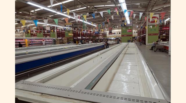 Un grupo de personas pasan delante de refrigeradores vacíos mientras hacen cola para comprar papel higiénico, detergente y arroz dentro de un supermercado Makro en Caracas. A veces, periódicos o usuarios de redes sociales confunden el caos que se desata e