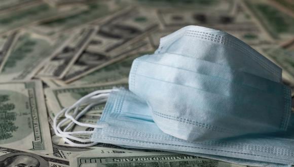 Medical face mask and dollar banknotes, world coronavirus finance, epidemic and economic losses concept. (Getty)