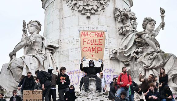 Un hombre sostiene un cartel que dice "Fuera Macron" mientras los manifestantes se paran en la estatua en la plaza Republique durante una manifestación una semana después de que el gobierno impulsara una reforma de las pensiones en el parlamento sin votación. (Foto de Emmanuel DUNAND / AFP)