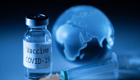 Una fotografía ilustrativa tomada el 19 de noviembre de 2020 muestra un vial con la etiqueta adhesiva de la vacuna COVID-19, una jeringa y un globo terráqueo.  (JOEL SAGET / AFP).