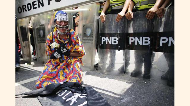 Una opositora del gobierno vistiendo un traje tradicional Wayuu se arrodilla frente a la policía antidisturbios que intenta evitar que la marcha de mujeres llegue a la Cancillería en Caracas, el 6 de mayo de 2017.(foto: Ariana Cubillos).