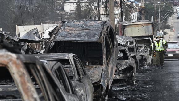 Carabineros chilenos pasan junto a vehículos quemados después de un incendio forestal en Quilpue, Viña del Mar, Chile, el 4 de febrero de 2024. (Foto de RODRIGO ARANGUA/AFP).