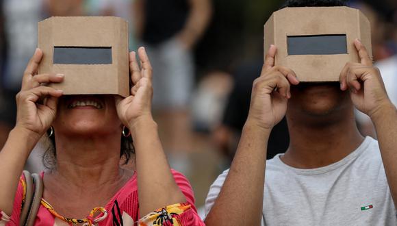 Dos personas protegiendo su vista con unos lentes especiales mientras observa un eclipse solar (Foto: AFP)