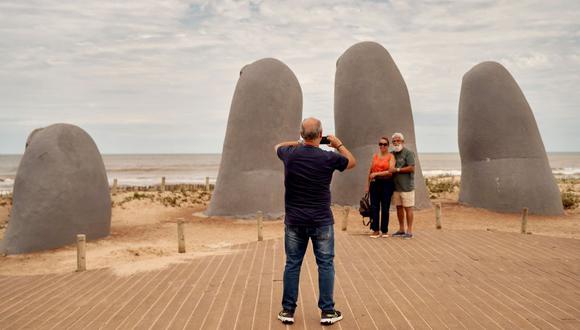 Turistas toman fotos frente a una escultura de una mano gigante que emerge de la arena en la playa Brava en Punta del Este, Uruguay, el sábado 19 de noviembre de 2022. Photographer: Ana Ferreira/Bloomberg