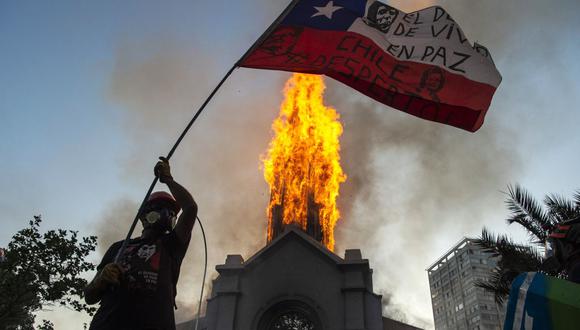 Un manifestante ondea una bandera de Chile frente a la Iglesia de la Asunción, que fue incendiada por encapuchados. (Foto de MARTIN BERNETTI / AFP).