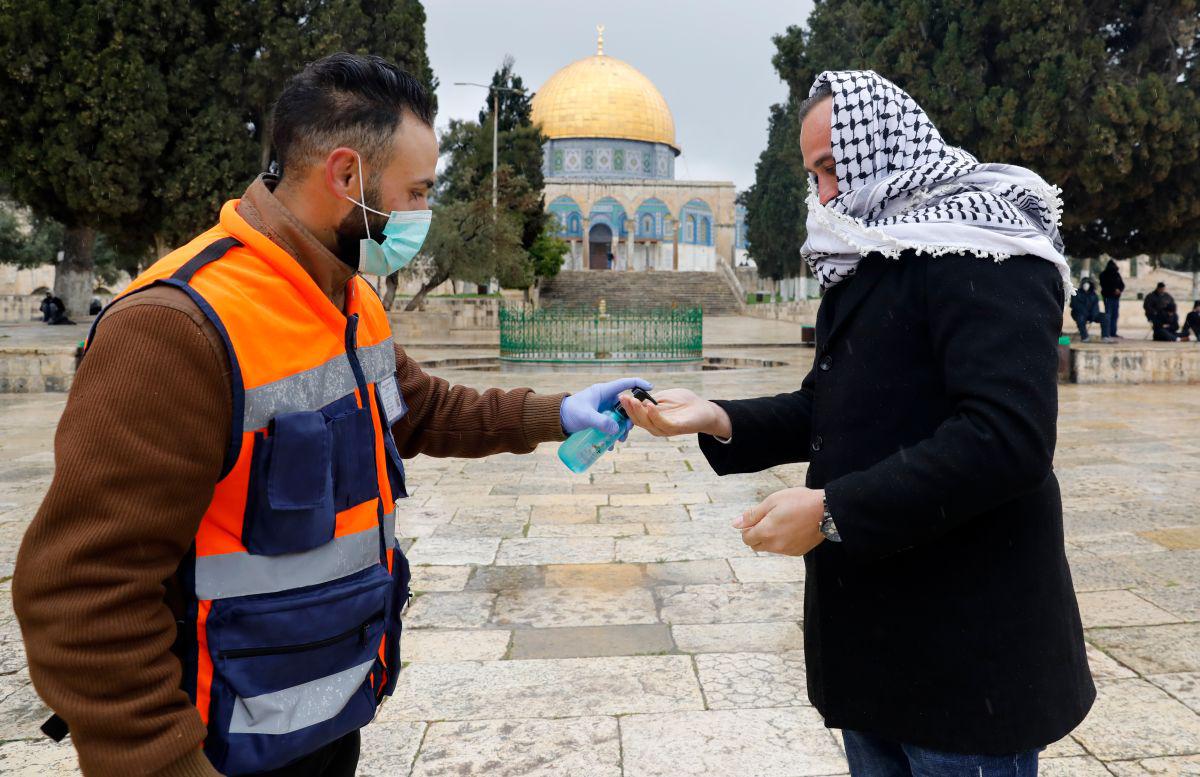 Un voluntario rocía gel desinfectante en las manos de un hombre palestino en su camino para realizar las oraciones en el complejo casi desierto de la mezquita Al-Aqsa en la Ciudad Vieja de Jerusalén. (Foto: AFP)