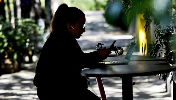 Una mujer mira su teléfono inteligente mientras está sentada en un restaurante, en la Ciudad de México, el 2 de febrero de 2023. (Foto de Pedro PARDO / AFP)