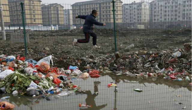 Un niño salta sobre un charco lleno de basura y deshechos, en una poblada villa de la localidad de Jiaxing, entre las más contaminadas del país. (Foto: William Hong)