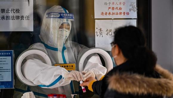 Un trabajador de la salud se prepara para tomar una muestra de hisopo de una mujer para detectar el Covid-19 en el distrito de Jing'an en Shanghai el 8 de diciembre de 2022.  (Foto por Héctor RETAMAL / AFP)