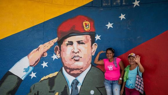 Dos mujeres posan para una fotogarfía junto a un mural de Hugo Chávez en Sabaneta, en el estado Barinas. (EFE/ Rayner Peña).
