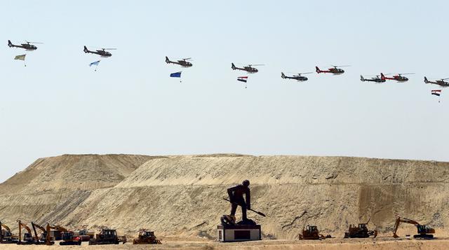 Helicópteros egipcios vuelan con banderas sobre una estatua de un hombre excavando y máquinas de construcción durante la ceremonia de inauguración del nuevo Canal de Suez en Ismailia, Egipto. El presidente de Egipto, Abdel Fattah al-Sisi, dio inicio el ju