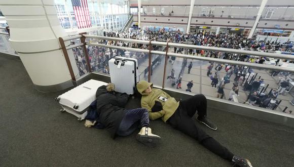 Un par de viajeros duerme mientras otros hacen cola abajo para pasar por el puesto de control de seguridad en el Aeropuerto Internacional de Denver en plena tormenta invernal en Estados Unidos. (Foto AP/David Zalubowski).
