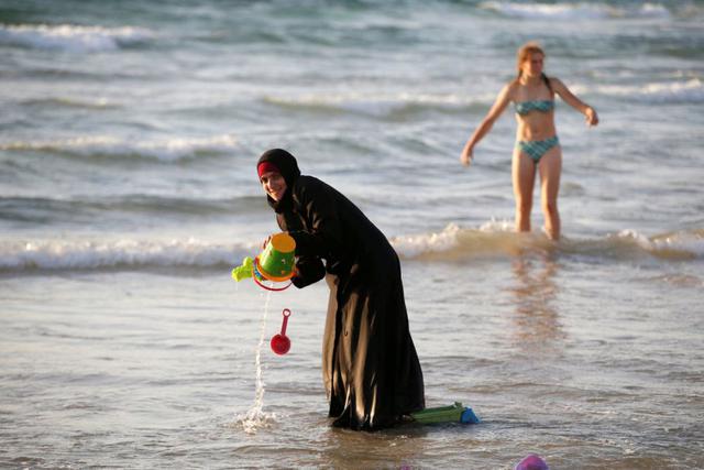 Una mujer musulmana que lleva un Hijab se coloca en las aguas en el mar Mediterráneo mientras que una chica israelí se mete en el agua con bikini. (Foto Reuters)