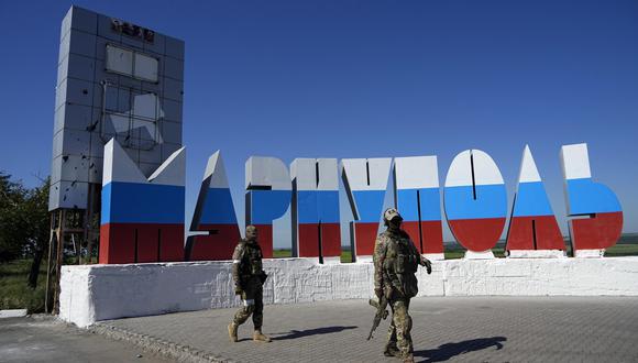 Soldados rusos pasan frente al nombre de la ciudad Mariúpol repintado con los colores de la bandera rusa en la entrada de Mariúpol, en Donetsk, en el este de Ucrania, el domingo 12 de junio de 2022. (Foto AP, Archivo)