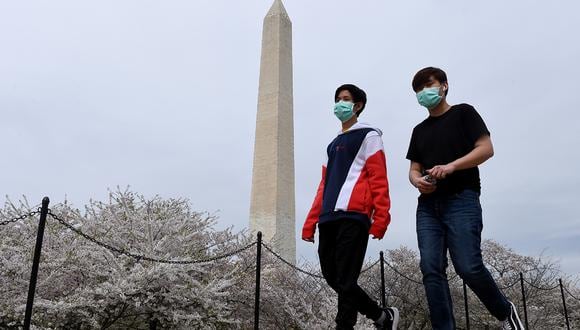 Dos jóvenes con mascarillas debido a la preocupación por la propagación del coronavirus pasan por el Memorial de Washington en el National Mall. (Foto: AFP)