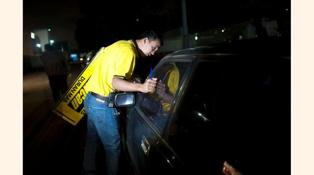 Un empleado de la tienda de baterías para autos Duncan toca la ventana del auto de un conductor, que espera en una fila desde la madrugada, para darle un ticket que le permitirá comprar una batería para su auto en la tienda ese día en Caracas, Venezuela. 