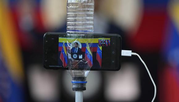 La imagen del líder de la oposición venezolana Juan Guaidó se ve en la pantalla de un teléfono celular dentro de una botella de plástico que lo sostiene firme mientras habla con la prensa en Caracas, Venezuela, el lunes 22 de noviembre de 2021, al día siguiente de las elecciones donde la abstención fue dominante y los aliados del gobierno del presidente Nicolás Maduro se adjudicaron el grueso de los cargos en disputa. (Foto AP/Ariana Cubillos).