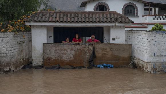 La gente mira detrás de un muro mientras el agua inunda la principal vía de acceso desde Lima al interior del país en los Andes luego de las fuertes lluvias en Chaclacayo, al este de Lima, Perú, el 15 de marzo de 2023. (Foto de Cris Bouroncle / AFP)