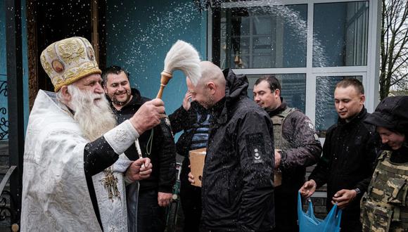 Los oficiales de policía reciben la bendición durante un servicio ortodoxo de Pascua con sonidos continuos de bombardeos a la distancia en la iglesia de San Pedro y San Pablo en Lyman, este de Ucrania, el 24 de abril de 2022. (Foto: Yasuyoshi CHIBA / AFP).