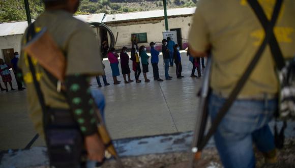 La gente hace cola para emitir su voto mientras la policía comunitaria monta guardia en un colegio electoral en la comunidad náhuat de Ayahualtempa, estado de Guerrero, México. (PEDRO PARDO / AFP)