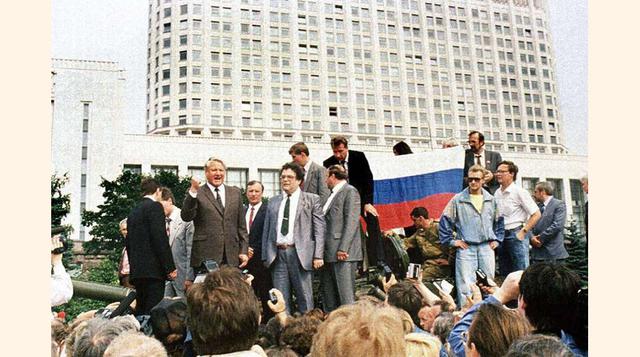 El presidente ruso, Boris Yeltsin, de pie encima de un vehículo militar ante el edificio de la Federación Rusa, en una imagen del 19 de agosto de 1991. A sus espaldas, varias personas sostienen una bandera de la Federación Rusa. Yeltsin se dirige a la mul