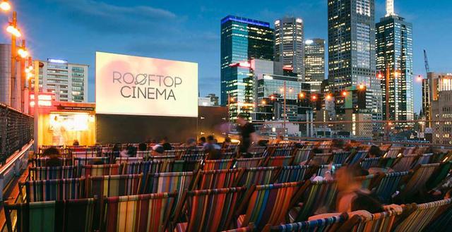 FOTO 1 | ROOFTOP CINEMA, AUSTRALIA. 185 sillas llenas de color y una pantalla gigante en la azotea de un edificio que permite ver una magnifica vista de Melbourne y sus rascacielos mientras se disfruta de una buena película bajo la luz de la luna.