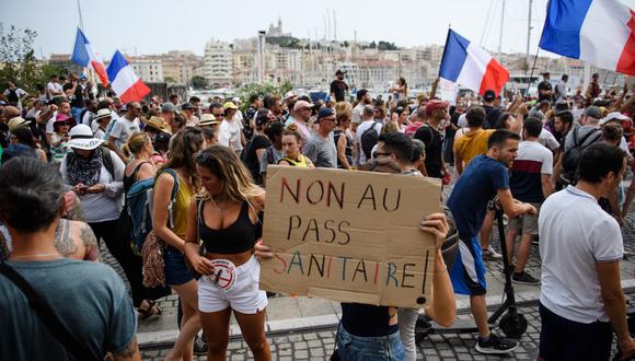 Un manifestante sostiene un cartel que dice "No al pase sanitario" mientras otros ondean banderas nacionales francesas durante una manifestación contra la vacunación obligatoria para ciertos trabajadores y el uso obligatorio del pase de salud convocado por el gobierno francés, en Marsella, sur de Francia, el 24 de julio de 2021. (CLEMENT MAHOUDEAU / AFP)