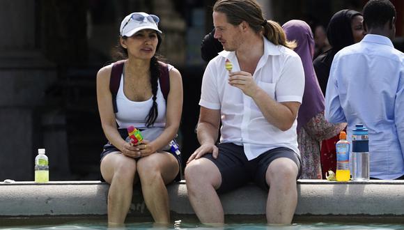 Una pareja toma un helado mientras se refresca sumergiendo los pies en la fuente de Trafalgar Square, en el centro de Londres, el 18 de julio de 2022. (Foto: Niklas HALLE'N / AFP)