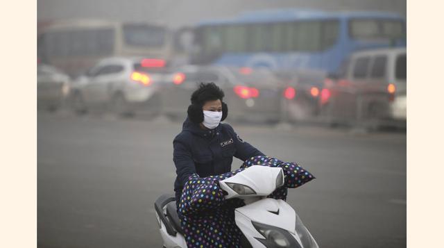 Una mujer china conduce su motocicleta cubierta con una máscara para evitar los efectos de la alta contaminación que existe en Beijing.