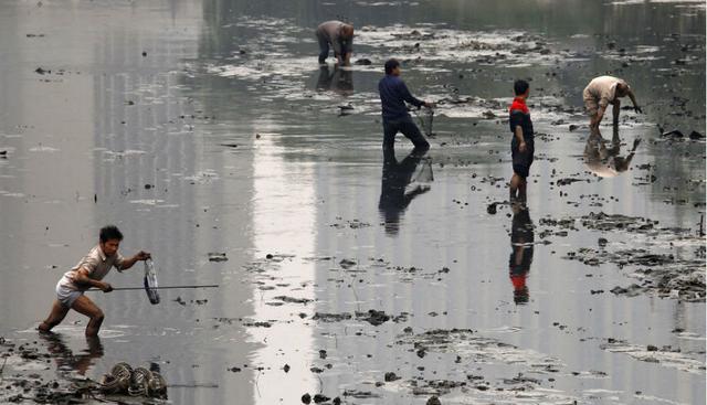 Unos pescadores intentan trabajar en un canal contaminado. Según la ‘OMS’, China multiplica el límite máximo de contaminación por veinte. (Foto: David Gray)