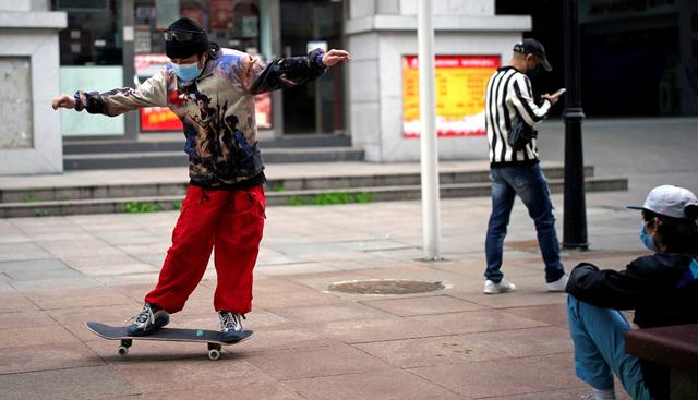 Un hombre con una máscara facial es visto con una patineta este sábado 28 de marzo en una calle de Wuhan, China. (Reuters).