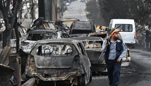 Un hombre pasa junto a vehículos quemados después de un incendio forestal en Quilpue, Viña del Mar, Chile, el 4 de febrero de 2024. (Foto de RODRIGO ARANGUA/AFP).