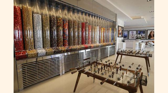 Una pared repleta de dispensadores de caramelos en el salón de la mansión, al lado de dos futbolines.