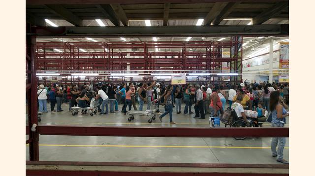 Los venezolanos hacen cola para comprar papel higiénico, detergente y arroz, junto a estantes vacíos dentro de un supermercado Makro en Caracas. Según la organización, que no ofreció cifras comparativas de años previos, casi seis veces a la semana se prod